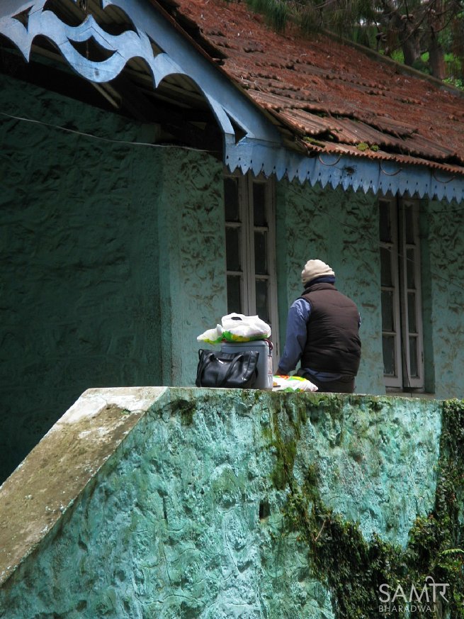 Man waits outside an old stone building with bags