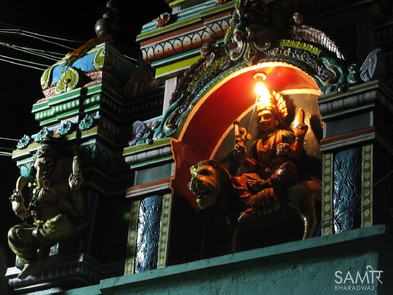 Decorative temple sculptures at night lit by street lights and an incandescent bulb